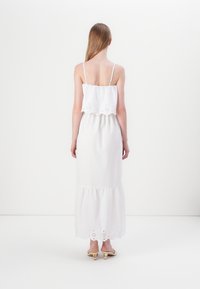 Hvit midi-kjole med justerbare stropper, lagdelt design og brodert bølgekant. Glatt stoff med en flytende silhuett.