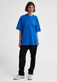 Blå bomullströja med korta ärmar och rund halsringning. Matchas med svarta avsmalnande byxor med vita sidostripes, och vita sneakers.