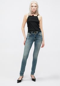 Μαύρο αμάνικο τοπ σε συνδυασμό με ανοιχτό μπλε στενό τζιν. Το τζιν έχει ένα ξεθωριασμένο εφέ. Τα υποδήματα περιλαμβάνουν μαύρες μυτερές γόβες.