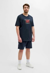 Marineblå bomulds t-shirt med et stort rødt og hvidt grafisk print på brystet, parret med matchende marineblå shorts og hvide sneakers.