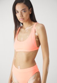 Neon narančasti bikini set koji uključuje sportsku bralette s okruglim izrezom i gaćice visokog struka. Izrađen od glatkog, rastezljivog materijala za udobnost.