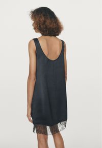 Zwart satijnen jurk met brede bandjes, een diepe U-vormige rug en kantafwerking aan de zoom. Soepele textuur met een vloeiend ontwerp en subtiele elegantie.