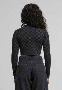 Fekete, hosszú ujjú, crop fazonú topp geometriai mintával, magas derekú sötét farmer nadrággal, zsebekkel.