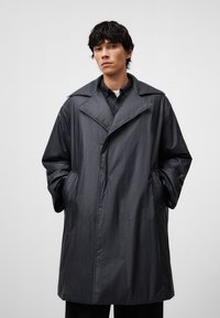 Długi, ciemnoszary płaszcz trench wykończony z lekkiego, gładkiego materiału. Posiada duży kołnierz, boczne kieszenie oraz prosty krój. Minimalistyczny design.