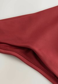 Rode stofmonster met een gladde textuur, voorzien van een gevouwen rand en fijne stiksels langs de naad. Eenvoudig ontwerp, zonder patronen of accenten.