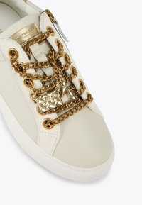 Sneaker bianco in pelle con dettaglio in catena dorata e charm. Presenta una superficie testurizzata e un design a punta rotonda. Chiusura con zip sul lato.