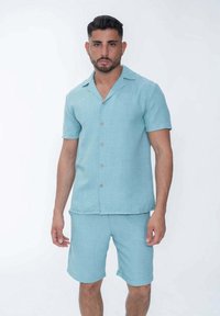 Chemise bleu clair à manches courtes avec un devant à boutons et un col, associée à un short assorti. Les deux pièces sont en tissu texturé.