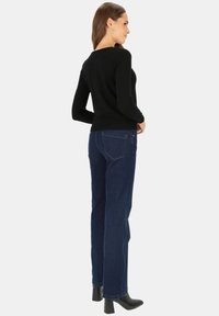 Czarna bluzka z długim rękawem w połączeniu z ciemnoniebieskimi spodniami o wysokim stanie, posiadającymi tylne kieszenie oraz czarnymi botkami na obcasie. Gładka tekstura materiału.