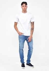 T-shirt bianco a maniche corte abbinato a jeans azzurri chiari. I jeans hanno un lavaggio sbiadito e delle sneakers nere completano l'outfit.
