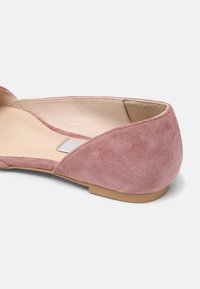 Chaussure plate en daim rose avec un talon arrondi, un design minimaliste, et une semelle intérieure lisse en cuir tan, présentant une texture subtile et sans aucun élément métallique visible.