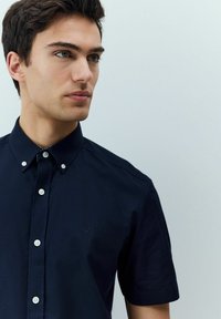 Marineblaues Kurzarmhemd aus Baumwolle mit einem Button-Down-Kragen, weißen Knöpfen und einem kleinen gestickten Logo auf der Brust.