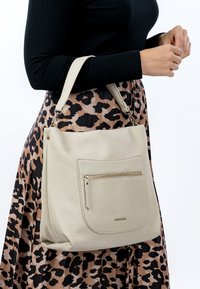 Light beige textured leather tote bag with a front zippered pocket and short strap, paired with a black ribbed top and leopard print skirt.