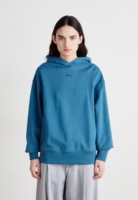 Felpa blu con cappuccio, dotata di tasca a marsupio frontale, caratterizzata da una vestibilità ampia, polsini a coste e un piccolo logo ricamato sul petto.