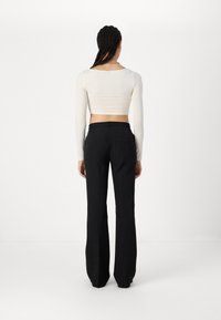 Un haut court à manches longues blanc associé à un pantalon évasé noir, présentant une texture lisse et des poches arrière. Vue arrière affichée.
