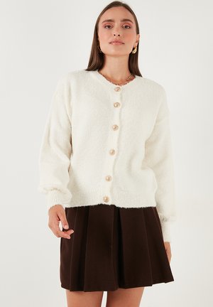 White, fluffy cardigan with a round neckline and long sleeves, featuring five large, patterned buttons down the front.