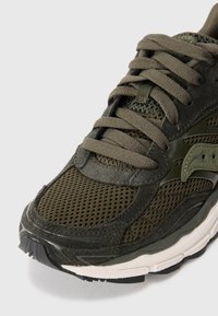 Green athletic shoe featuring mesh and suede materials, round toe, textured surface, and flat laces with a cushioned sole and black accents.