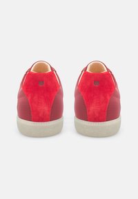 Rote Sneakers mit einer Kombination aus glattem und Wildleder-Texturen, mit abgerundetem Zehenbereich, gepolstertem Kragen und gemusterten Akzenten an den Seiten.