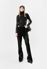 Top negro ajustado con mangas largas y cuello alto, combinado con pantalones negros de tiro alto que presentan detalles en cuero y un diseño minimalista.