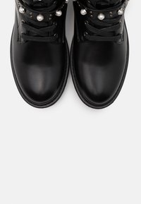 Bottines en cuir noir avec bouts ronds, ornées d'accents en perles et d'un design à lacets, sur fond blanc.