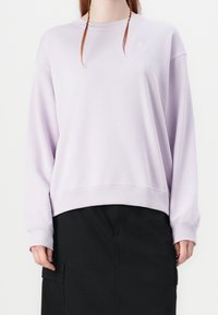 Lichtpaarse sweatshirt met ronde hals, geribbelde zoom en manchetten; heeft een klein wit logo op de borst. Gecombineerd met een zwarte rok.