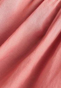 Měkká látka v jemné korálové barvě, s hladkou texturou a jemným leskem, vytvářející měkké záhyby a vlnění.