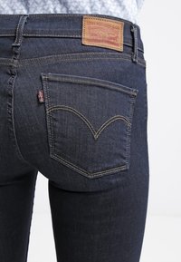 Jeans de mezclilla azul oscuro con costuras visibles en los bolsillos traseros, una pequeña etiqueta roja de Levi's y un parche de cuero marrón de Levi Strauss & Co.