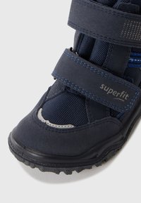 Detailní záběr dětské tmavě modré boty na suchý zip značky "superfit", s texturovanou tkaninou a gumovou podrážkou.