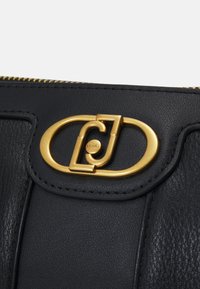 Borsa in pelle nera con superficie texturizzata, caratterizzata da un accentuato hardware ovale dorato nella chiusura e una zip nella parte superiore.