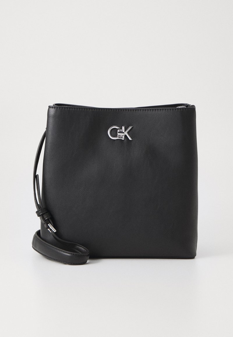 Borsa a mano in pelle nera con un design elegante. Presenta un logo argentato, una tracolla regolabile, chiusura con zip e superficie liscia.