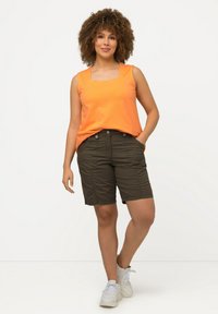 Top arancione senza maniche con scollatura quadrata, abbinato a pantaloni corti verde scuro con tasche e chiusure a bottone. Sneakers casual completano il look.