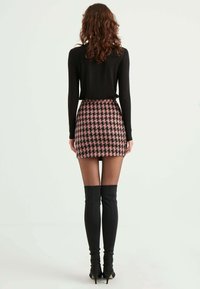 Schwarzes Langarmoberteil, gemusterter rosa karierter Minirock und über-die-Knie hohe schwarze Absätze. Glatte Textur mit taillierter Silhouette und betonter Taille.