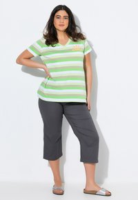 Relaxed fit V-hals T-shirt van gestreept groen en wit stof, gecombineerd met grijze cropped broek. Opvallende zon graphic detail op het shirt.