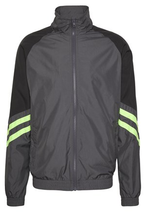 Sort og grå vindjakke med høj krave, lynlås foran, elastiske manchetter og to grønne striber på ærmerne. Letvægts, sporty design.