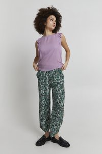 Blusa viola senza maniche con spalle arricciate abbinata a pantaloni neri larghi con una piccola stampa floreale in rosa e bianco. Scarpe nere.