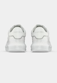 Ténis brancos com parte superior em couro liso e sola espessa de borracha. Apresentam calcanhar arredondado, marca em relevo no calcanhar e colarinho acolchoado.