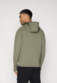 Χακί πράσινη φούτερ με κουκούλα, με ομαλή υφή και ραφές, εμφανιζόμενη από πίσω. Διαθέτει εφαρμοστή σχεδίαση με μακριά μανίκια.