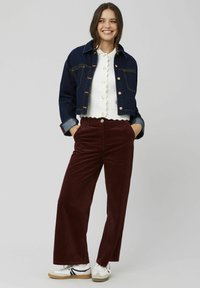 Veste en denim foncé raccourcie avec des boutons dorés, top blanc à volants et pantalon large en velours côtelé bordeaux associé à des baskets blanches.