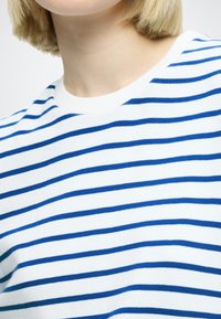 Pull en coton blanc avec des rayures horizontales bleues. Encolure arrondie avec texture côtelée. Tissu doux au design décontracté.