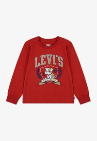 Piros, hosszú ujjú pamut póló, amelyen egy kutya grafika, a "LEVI'S" felirat és díszes babérmotívumok találhatók. Oldalt cimke.