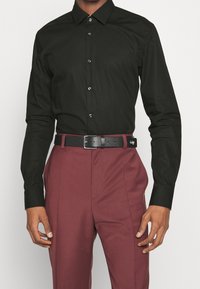 Camicia nera con maniche lunghe, abbinata a pantaloni bordeaux e una cintura nera con fibbia in argento e un accento del logo.