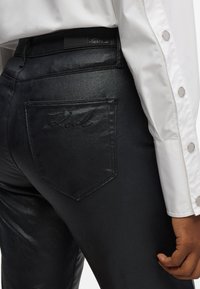 Μαύρα τζιν παντελόνια με ελαφριά γυαλάδα, που διαθέτουν μία κομμένη λογότυπο στην πίσω τσέπη και μία δερμάτινη ετικέτα με λογότυπο στη ζώνη.