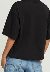 Černé zkrácené tričko s krátkými rukávy, vyrobené z bavlny. Má hladkou texturu a jednoduchý, pohodlný design.