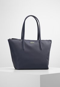 Navy blue leather tote bag with two long handles, textured surface, zip closure, and a small embroidered logo on the front.