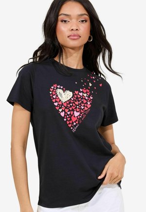T-shirt noir avec un graphique de cœur composé de cœurs rose et crème, accompagné du texte "Portez-le avec amour" en dessous. Manches courtes, coupe décontractée.