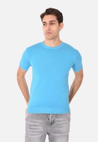 Maglione azzurro chiaro a maniche corte con colletto rotondo, realizzato in tessuto a maglia, caratterizzato da una texture liscia e polsini e orlo a coste. Indossato con jeans grigi.