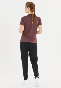 Bordeauxrotes Kurzarmhemd kombiniert mit schwarzen Jogginghosen. Das Outfit zeichnet sich durch eine lockere Passform, eine sanfte Textur und elastische Bündchen an den Hosen aus.