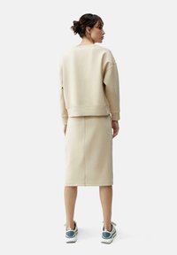 Beige sweatshirt and skirt set made of soft fabric; relaxed fit; features ribbed cuffs and a knee-length skirt with subtle stitching detail.