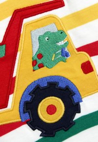 Gesticktes Design mit einem grünen Dinosaurier in einem gelben Truck mit roten Punkten, blauen Rädern und einem gestreiften Hintergrund in Rot, Gelb und Grün.