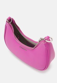 Petit sac à main courbé de couleur rose vif avec une fermeture éclair argentée partiellement ouverte et une plaque au nom de la marque argentée à l'avant.