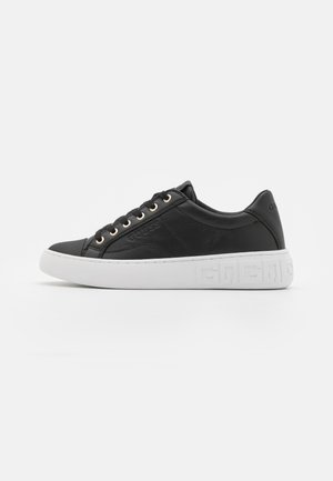 Sort læder sneaker med hvid præget sål, snørebånd foran med guldøjer og diskret mærkelogo på siden og hælen.